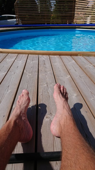 Person som sitter på trädäck med fötterna synliga framför en pool för avkylning under byggprojekt.