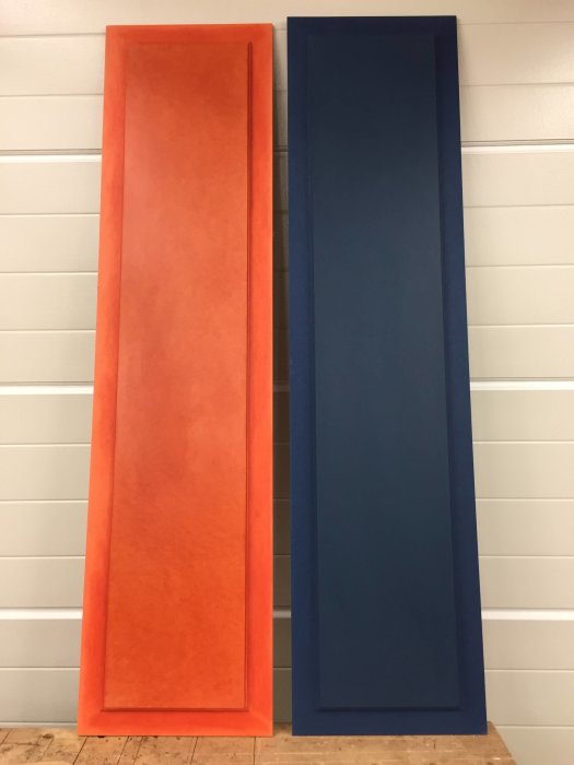 Två stora, stående, rektangulära paneler i orange och blått lutade mot en vit vägg.