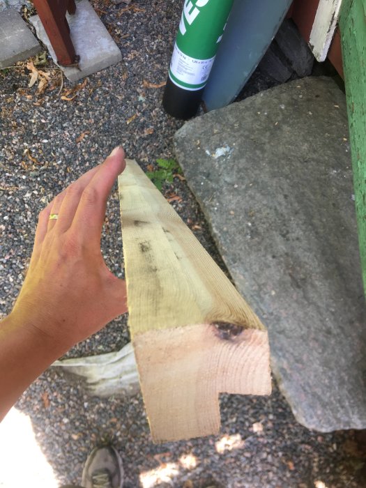 Hand håller ett sågat trästycke med en utstickande läpp, avsett för byggkonstruktion.