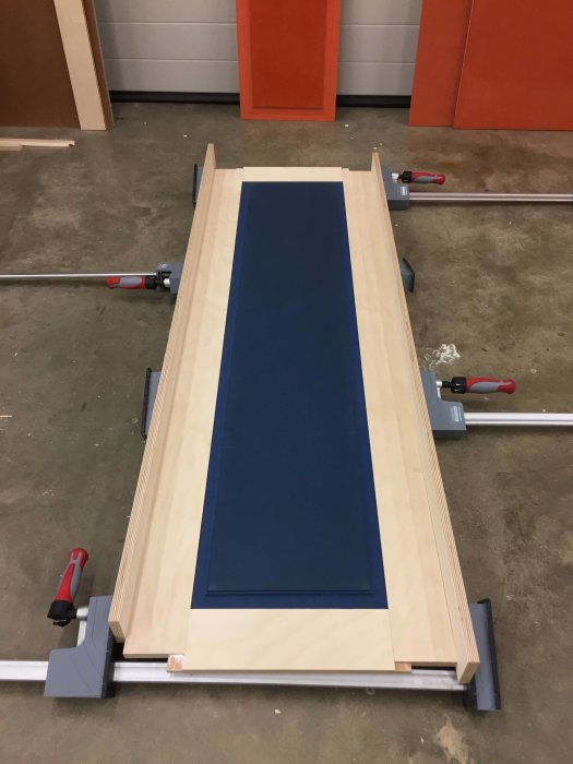Träpanel till dörr i klämskruvar på arbetsbänk, redo för att sågas och fräsas.