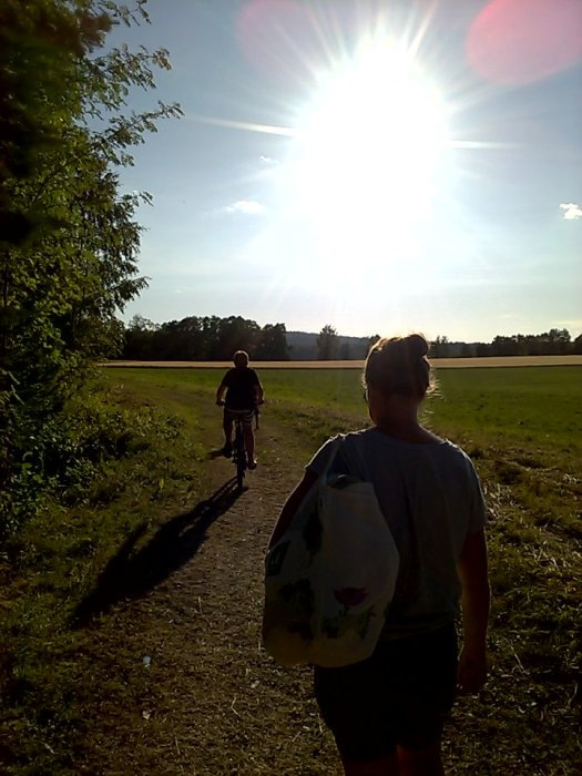 Person går på en stig mot solnedgången med en handduk, en annan cyklar framför.