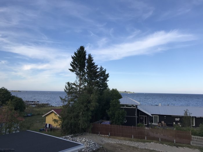 Vy över hustak med hav och himmel i bakgrunden och träd som ramar in bilden.