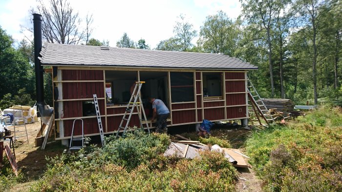 Renovationsarbete på hus med ny yttervägg och plats för fönster, omgivet av natur.