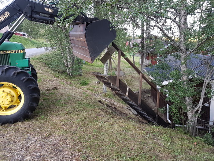 Traktor gräver nära en lutande trätrapp som leder till en stuga, för att justera instabila plintar under.