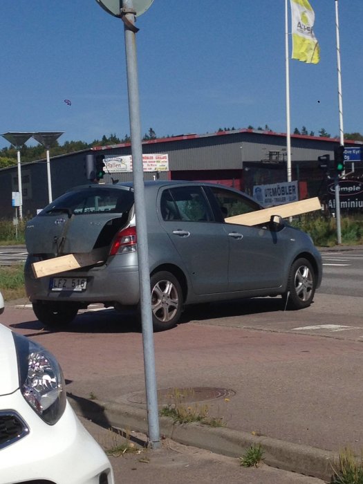 Bil med ett stort trästycke fastklämt vid sidodörren parkerad på gata.