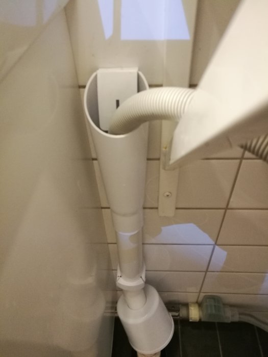 Tvättmaskins avloppsslang ansluten till vertikalt grått avloppsrör med synlig läcka.