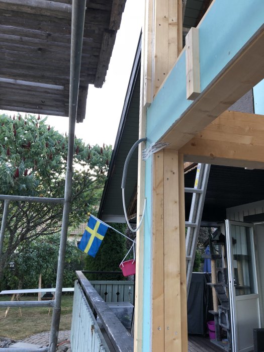 Renoveringsarbete på en altan med nya läkt och reglar under konstruktion och en svensk flagga i bakgrunden.