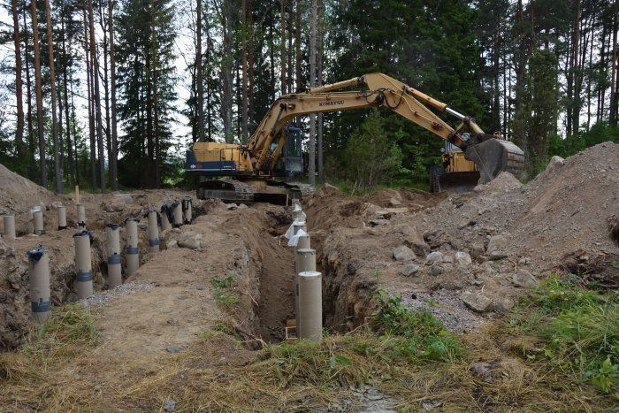 Nybyggd rad av betongplintar på byggplats med grävmaskin och uppgrävd mark i bakgrunden.