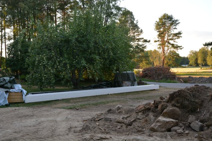 Nybyggd bottenplatta med limträbalkar på ett byggprojekt, omgiven av grus och schaktmassor.