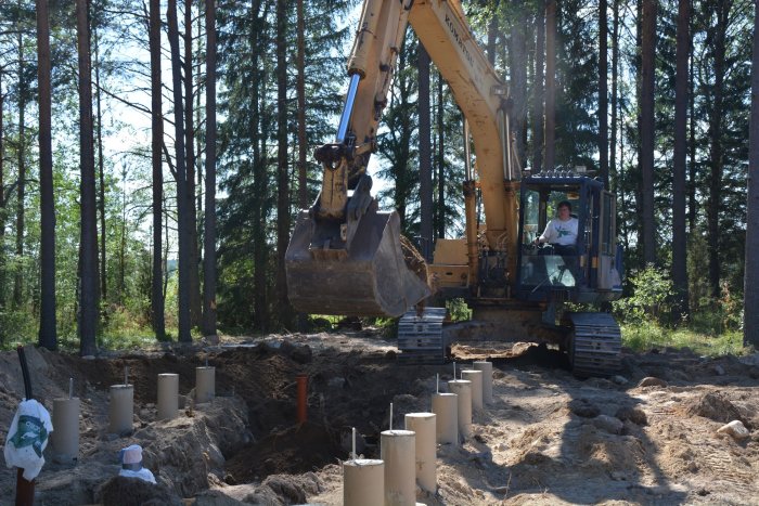 Grävmaskin i arbete med att återfylla mark runt nygjutna plintar för byggprojekt.