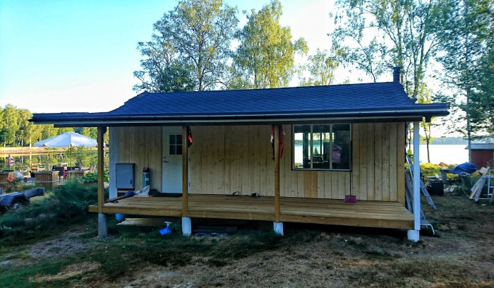 Nybyggd veranda på stuga med grundmålade fasadbrädor och utsikt över vatten.