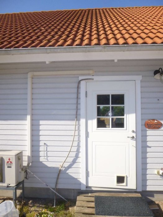 En enkel lösning för att leda ner regnvatten med en provisorisk ränna längs en husvägg och en vit dörr.