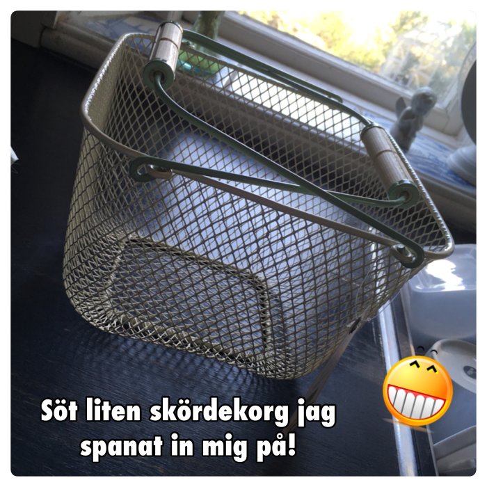 Liten metallisk skördekorg med handtag på fönsterbräda.
