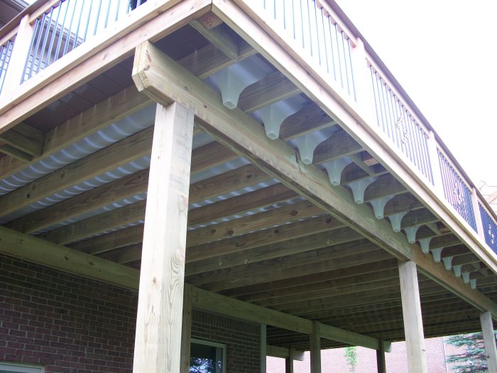 Balkong med träkonstruktion ovanpå uterum, visar under deck drainage system med vattensamlande plåtar under tralldäck.