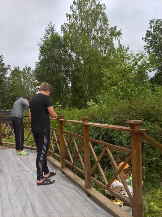 Två tonåringar som arbetar på en träaltan med skyddsplast på golvet och grönska i bakgrunden.