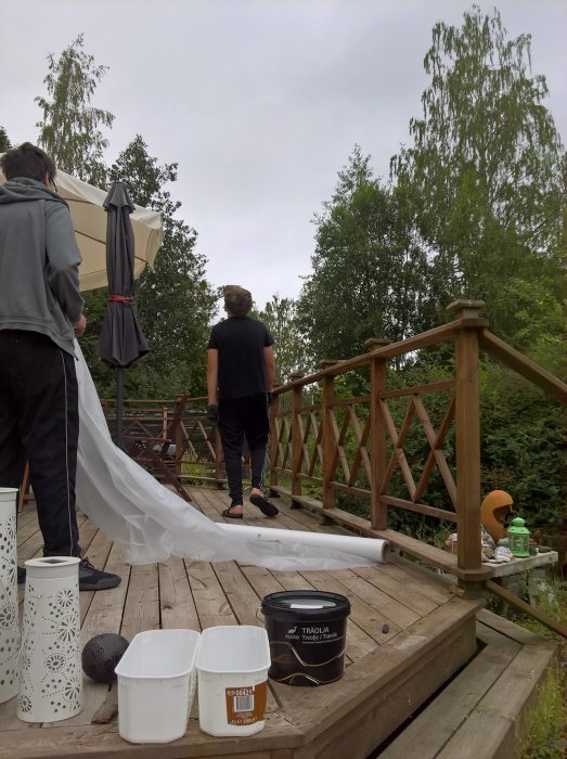 Två personer på en träaltan med målarutrustning och en utvikbar segelduk.