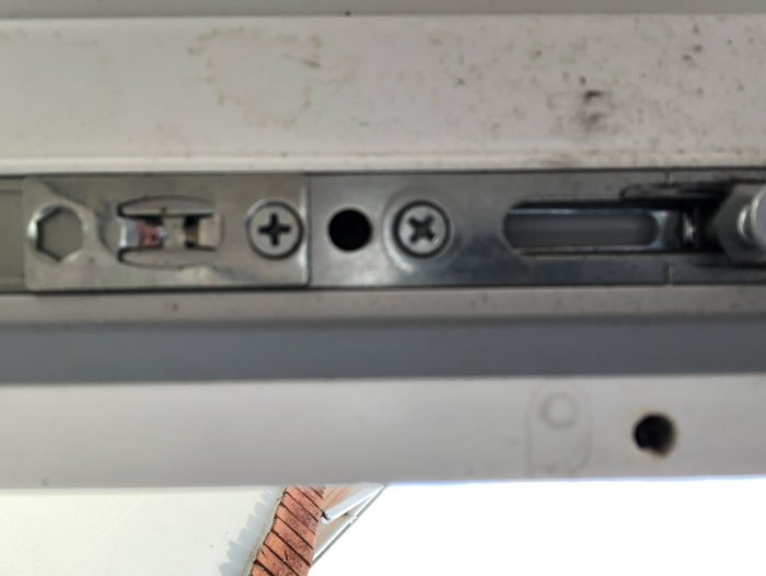 Undersida av balkongdörr med lås och skruvar, fotograferad inifrån.