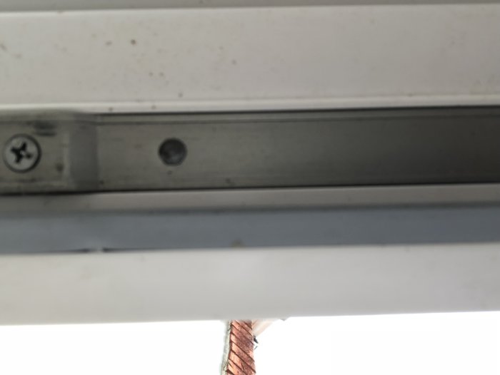 Undersida av balkongdörr med synlig skruv och metallfäste, fotograferad inifrån.