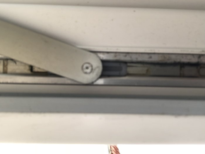 Undersida av balkongdörr med synliga gångjärn och spår av korrosion, tagen inifrån.