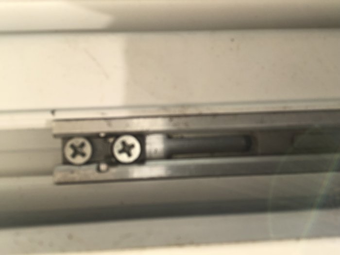 Närbild av låsmekanismen på undersidan av en balkongdörr inifrån en lägenhet, med fokus på skruvarna.