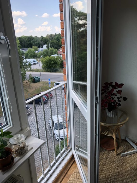 Öppen balkongdörr från insidan av en lägenhet med lås synligt, utsikt över parkeringsplats och träd.