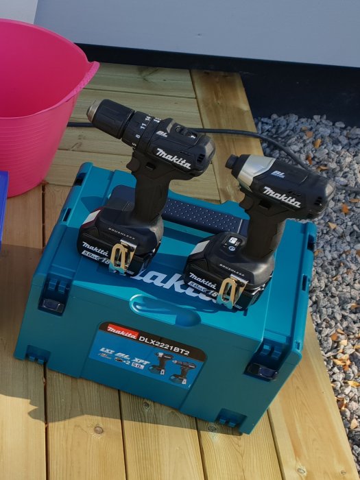 Makita DLX2221BT2 verktygskit med borrskruvdragare och slagmutterskruv på blå förvaringslåda utomhus.