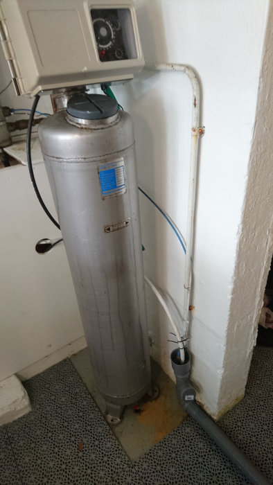 Ett filtersystem bestående av en silverfärgad filtercylinder och en syreaktivator monterad på toppen, med anslutna rörledningar.