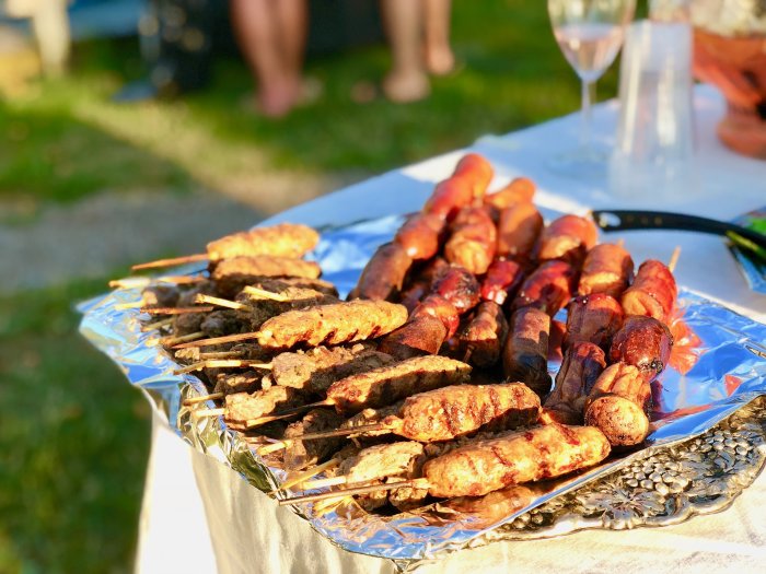 Fat med olika grillspett, inklusive köftaspett och korv, serverade utomhus med en suddig bakgrund.