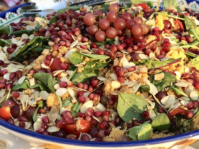 Färgstark couscoussallad med granatäpple, vindruvor, mandelflarn och gröna blad på blå fat.