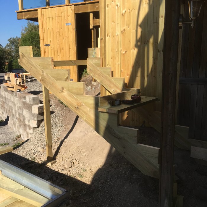 Träkonstruktion av en oavslutad utetrappa med verktyg som visar mått och vinklar under uppbyggnad.