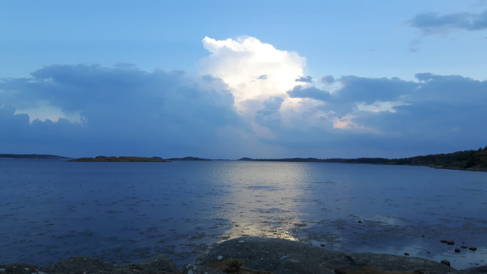 Dramatiska åskmoln över havet vid skymning med reflektioner i vattnet.