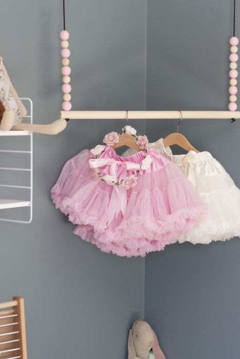 Inredd barnkammare med rosa och vita prinsessklänningar på klädhängare mot blå vägg.