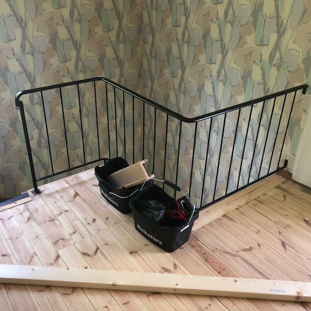 Bild på en hall under renovering med ett svart metallräcke, verktygslådor och ombonat trägolv.