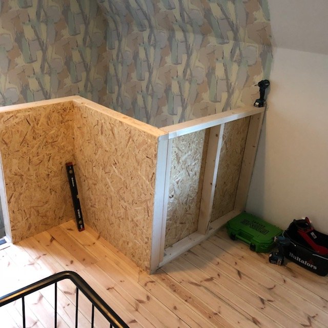Nybyggt trä- och gipsräcke i en hall under konstruktion med verktyg vid sidan.