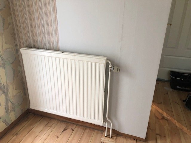 Renoveringstapet applicerad över masonit i hörn av hall med vit element och trägolv.