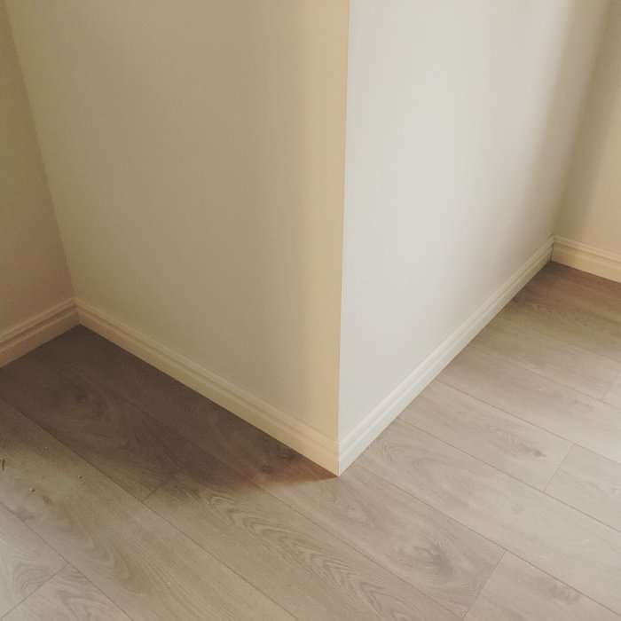 Nyinstallerade vita golvsocklar i ett hörn med beige väggar och grått laminatgolv.