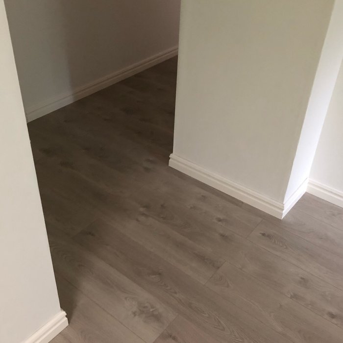En nyrenoverad korridor med snyggt laminatgolv och vita golvsocklar längs väggarna.