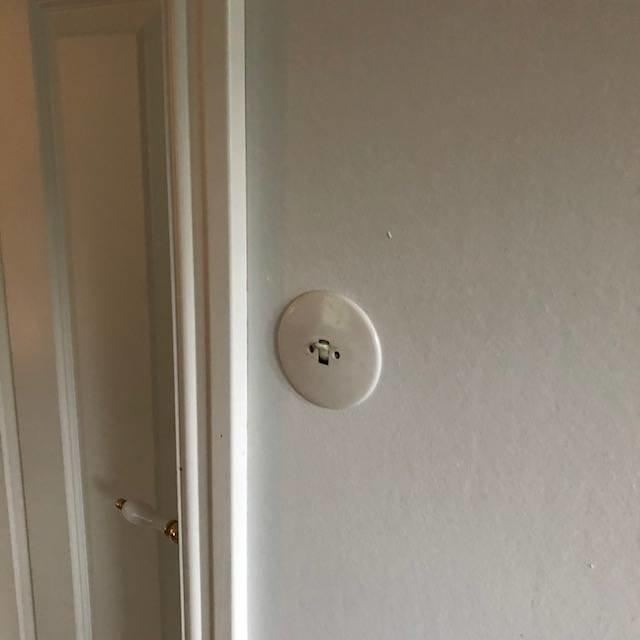 En nyinstallerad vit strömbrytare på en ljus vägg med dörrkarm och handtag i bakgrunden.