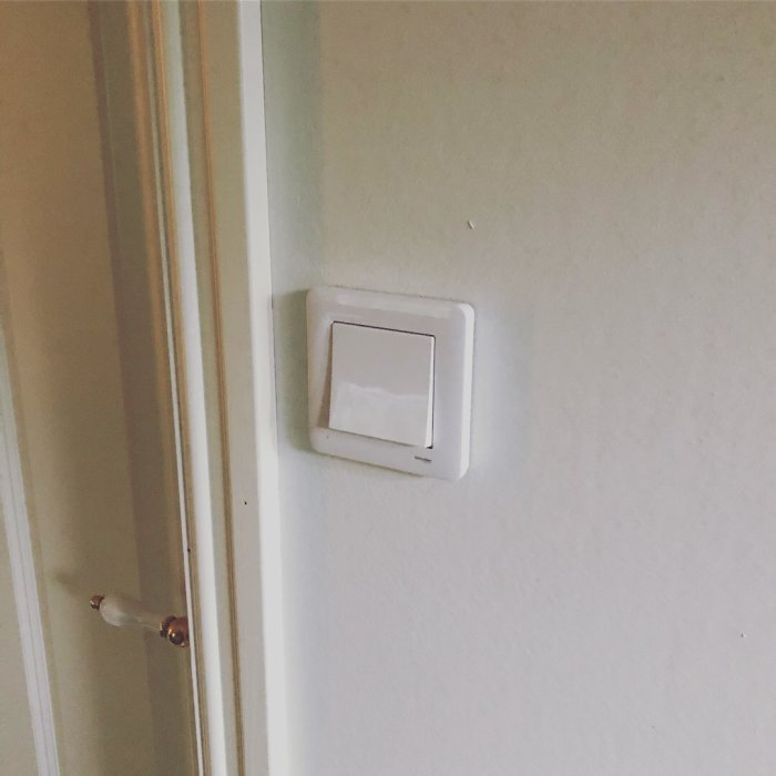 Nyinstallerad vit strömbrytare på en texturerad vägg bredvid en dörr med träfoder och lister.