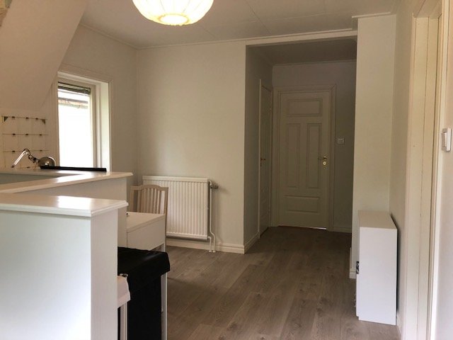 Renoverat rum med köksö, vit skåpinredning, trägolv och en stängd dörr. #återbruk #renovering