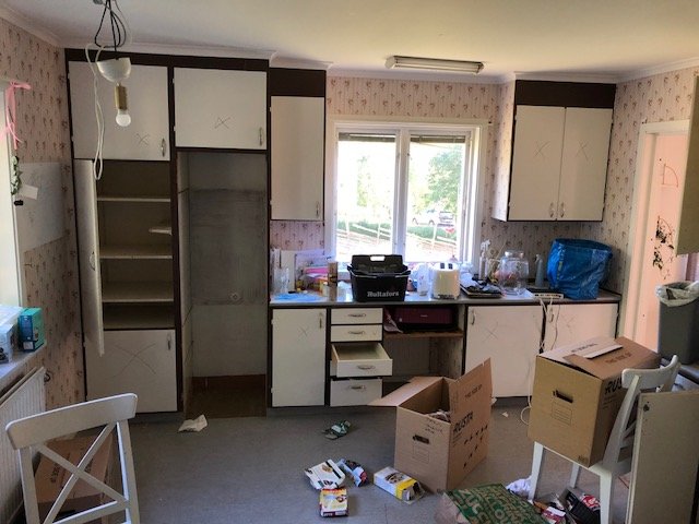 Ett kök under renovering med gamla skåp och kartonger utspridda på golvet.