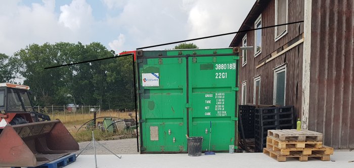 En grön container står framför en lada med ritade linjer som visar planerat tak och skydd.