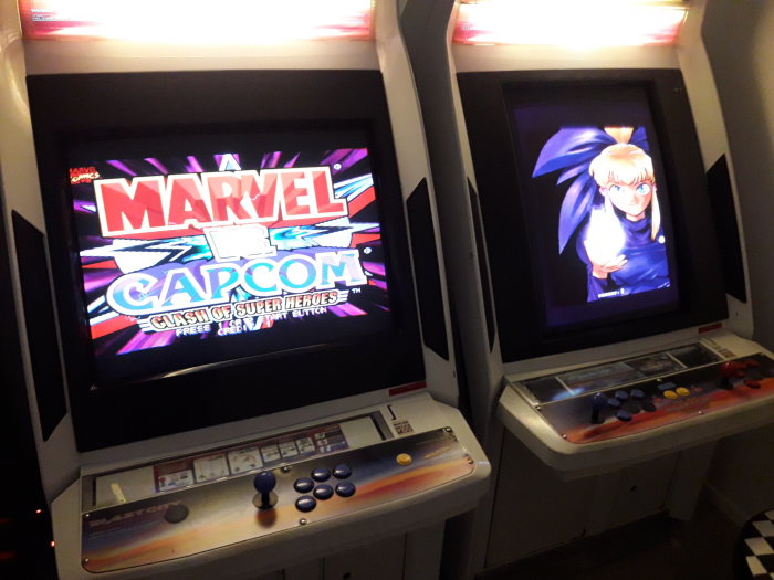 Två arkadspelmaskiner med CRT-skärmar som visar spelet 'Marvel vs. Capcom' och karaktärsbild.