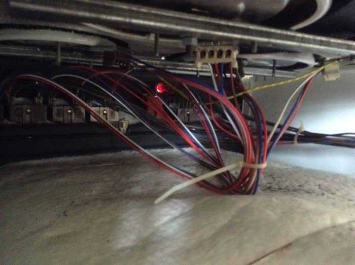 Elinstallation med flertal färgade kablar, några anslutna till dosor, under ett spisutrymme.