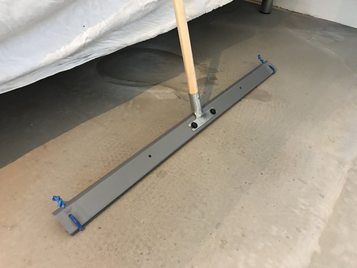 Egentillverkad skrapa av bärlist med kabelstumpar som distanser används på ett betonggolv.