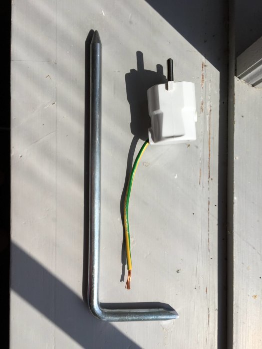 Jordspett och avklippt elkabel med exponerade gröngula trådar placerade på en ljus yta.