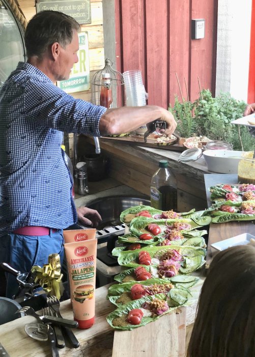 Man förbereder ost- och jalapeñofyllda burgare och serverar dem med sallad och tillbehör på ett utomhuskök.