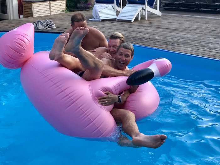 Tre personer har roligt och flottar i en pool på en uppblåsbar flamingo.