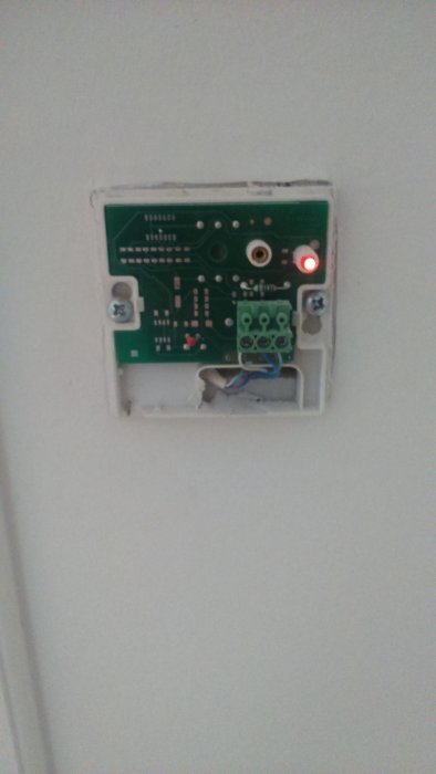 En öppen väggmonterad dosa med elektronisk kretskort och en blinkande röd diod.