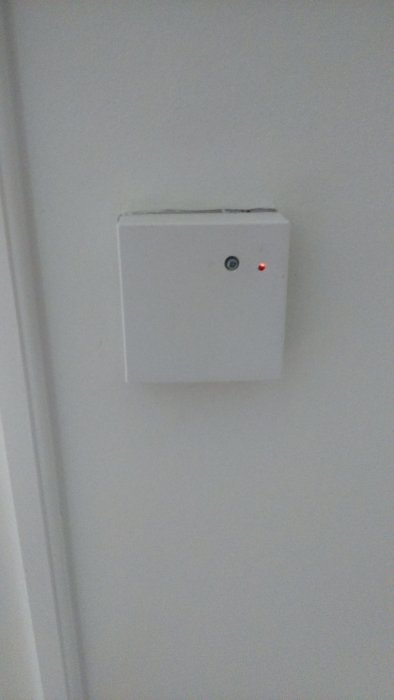 Liten vit dosa på vitt vägg med en röd blinkande diod.